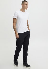 Hvit kortermet t-skjorte kombinert med svarte bukser. Svarte joggesko med hvite såler. Enkelt design, jevn tekstur og tettsittende fasong.