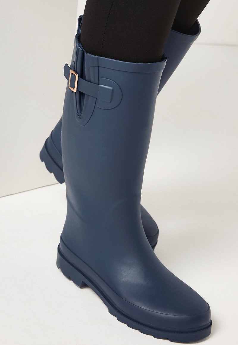 Marineblauwe rubberen regenlaarzen met een matte afwerking, voorzien van een decoratieve riem en gesp, een ronde neus en een gestructureerde zool voor grip.