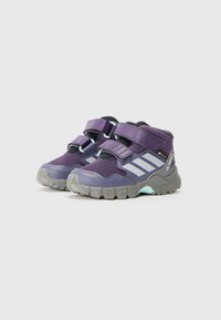 Lila High-Top-Schuhe mit grauen Sohlen, ausgestattet mit zwei verstellbaren Klettverschlüssen und seitlichen Streifen. Entworfen für Langlebigkeit und Komfort.