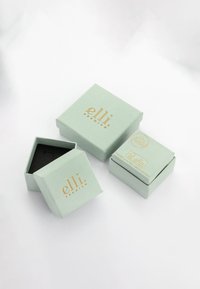 Trois boîtes à bijoux vert clair avec un texte doré "elli premium", une ouverte montrant un intérieur noir, sur une surface blanche.