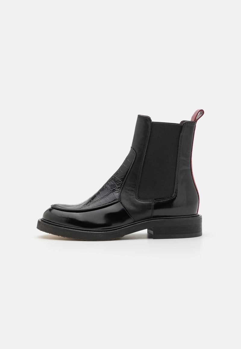 Botte Chelsea en cuir noir avec texture crocodile à l'avant, panneaux latéraux élastiques, petit talon et languette rouge à l'arrière.