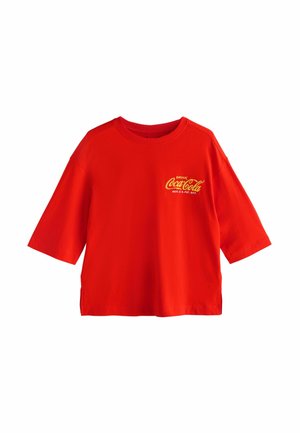 Punainen lyhythihainen puuvillainen t-paita, jossa edessä keltaisella teksti "DRINK Coca-Cola". Yksinkertainen, löysä malli, jossa pyöreä pääntie.