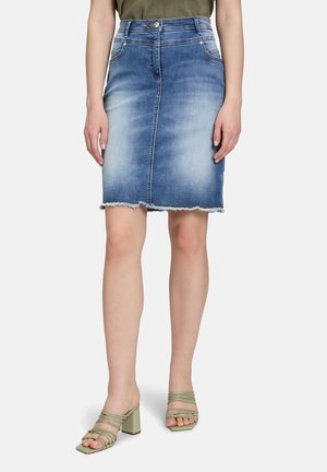 Jupe en denim de type crayon avec délavage, ourlet brut, poches avant et taille haute. Associée à des sandales à talons vertes.