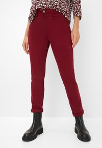 Pantalons slim fit bordeaux avec ourlets roulés, fabriqués en tissu doux en mélange de coton. Associés à des bottines noires pour un contraste.
