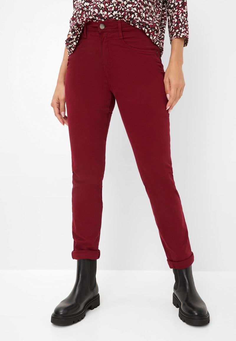 Pantalons slim fit bordeaux avec ourlets roulés, fabriqués en tissu doux en mélange de coton. Associés à des bottines noires pour un contraste.