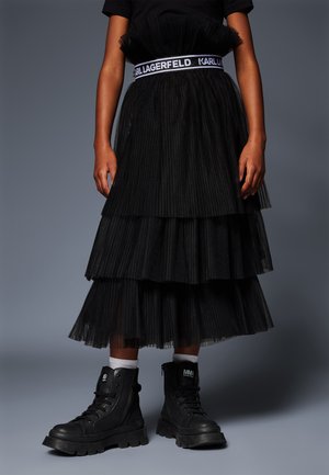 Une jupe en tulle noir à couches featuring une taille large avec la marque "Karl Lagerfeld", associée à des bottes de combat noires et des chaussettes blanches.