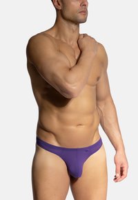 Lila Herren-Tanga, aus weichem Stoff gefertigt. Verfügt über eine glatte Textur, einen niedrigen Bund und ein Design mit minimaler Abdeckung.