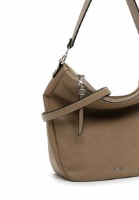 Sac à main en cuir beige avec une forme incurvée, une fermeture éclair sur le dessus et une seule bandoulière. Présente des accessoires en argent et des détails de couture subtils.