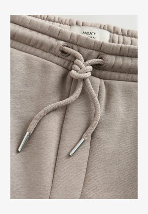 Beige joggingbroek tailleband met een gestrikte trekkoordknoop en een zichtbaar merklabel aan de binnenkant van de tailleband met de tekst "NEXT".