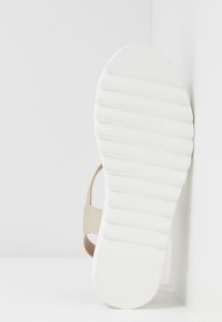 Beige szandál texturált talprésszel és fehér bordázott talppal, amely egyszerű dizájnt és minimális fém elemeket mutat be. 38-as méret jelölve.