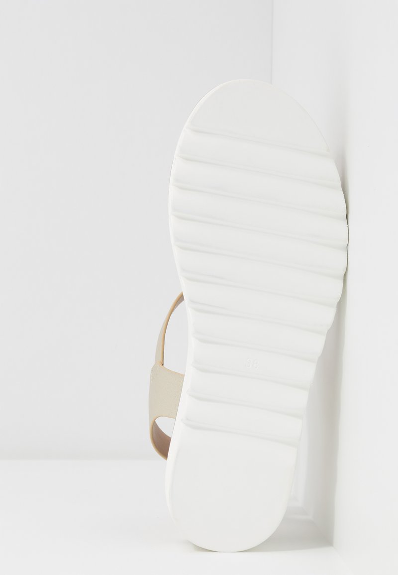 Sandale beige avec une semelle intérieure texturée et une semelle extérieure blanche à striures, mettant en avant un design simple et des éléments matériels minimaux. Taille 38 marquée.