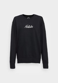 Černá mikina vyrobená z bavlny s klasickým kulatým výstřihem, s bílým vyšitým logem "Hollister" na hrudi a žebrovanými manžetami.