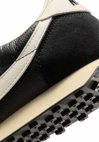 Zwart-crème sneaker met een bovenwerk van leer en suède, een gestructureerde tussenzool en een rubberen buitenzool met een profiel voor grip.