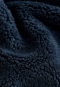 Couverture en peluche bleu marine avec une surface douce et texturée, présentant des fibres denses et duveteuses ainsi qu'une apparence légèrement froissée.