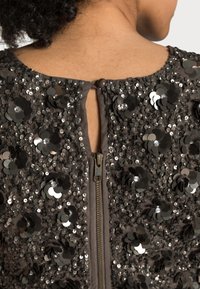 Top con paillettes con scollatura rotonda e chiusura con zip sul retro. Caratterizzato da paillettes argento metallizzato e nere disposte in motivi floreali.