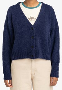 Mörkblå, mjuk kofta med V-ringning, långa ärmar och sex svarta knappar framtill. Ribbad fåll och ärmslut; kort modell.