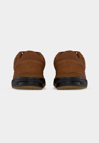 Καφέ αθλητικά παπούτσια με επάνω μέρος από υφασμένο σουέντ, μαύρη λαστιχένια σόλα και ραμμένες διακοσμήσεις. Πλάγια όψη που τονίζει το σχεδιασμό της φτέρνας.