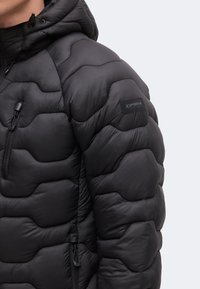 Veste matelassée noire avec capuche, poche zippée sur la poitrine, fermeture éclair et patch de marque sur la manche supérieure.