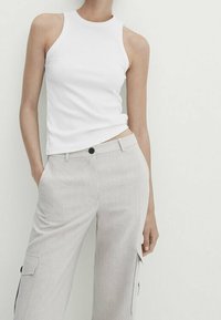 Witte mouwloze geribbelde tanktop gecombineerd met lichtgrijze cargobroek met zijzakken en een enkele knoopsluiting.