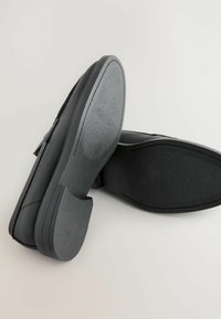 Sorte lædersko med struktureret overflade, der har en glat gummisål og en let hævet hæl. Designet er minimalistisk og funktionelt.