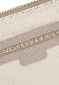 Bolsa beige texturizada con un patrón de espiga diagonal, con un detalle en cuero gris y una cremallera dorada para un cierre seguro.