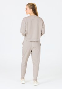 Sweatshirt gris clair et joggings assortis, fabriqués en tissu doux. Présente un design légèrement court avec une coupe décontractée et des poches latérales.