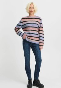 Pull en tricot rayé dans des teintes pastel de rose, bleu et noir, avec un col rond et des poignets côtelés, associé à un jean skinny bleu et des bottes noires.