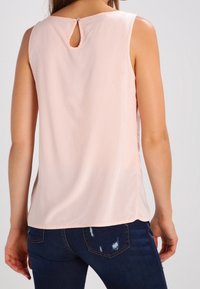 Top sin mangas de color rosa claro con un corte en forma de llave en la parte posterior, hecho de una tela suave, combinado con jeans de mezclilla oscura con un diseño desgastado.