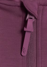 Gros plan d'une fermeture éclair violette avec un curseur de marque sur un vêtement en tissu assorti, montrant la texture et les coutures détaillées.