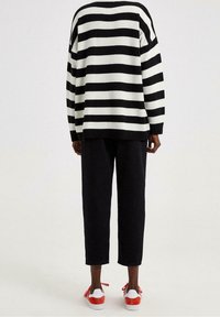 Sort-hvid stribet oversized sweater i strikstof, kombineret med sorte cropped bukser og sneakers med røde detaljer.