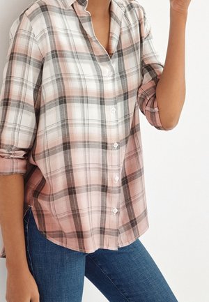Chemise à carreaux rose clair et gris avec un col, des manches retroussées et un ourlet légèrement arrondi, faite d'un tissu doux. Jeans visibles en dessous.