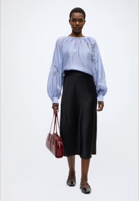 Ανοιχτό μπλε μπλούζα με φουσκωτά μανίκια και κεντήματα με λουλούδια, συνδυασμένη με μαύρη σατέν μίντι φούστα και μαύρα μπαλαρίνες. Λεπτομέρεια με κόκκινη τσάντα.