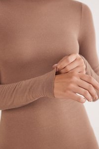 Langærmet, tætsiddende top i blødt, lysebrunt stof. Har sømløse ærmer og høj hals, som fremhæver den glatte tekstur og den kropsnære pasform.