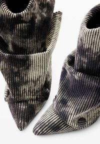 Botas de punta afilada hechas de tela acanalada, con un esquema de color en gris oscuro y crema, con puños doblados y costuras destacadas.