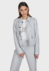 Light gray cropped jacket with a collared neckline and front buttons, paired with a white T-shirt featuring silver glitter text.