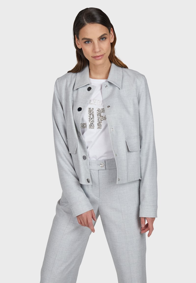 Light gray cropped jacket with a collared neckline and front buttons, paired with a white T-shirt featuring silver glitter text.