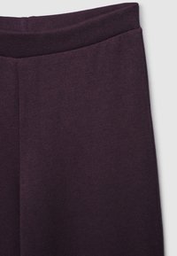 Pantaloni in tessuto a maglia viola scuro che mostrano l'elastico in vita e la sezione superiore della gamba con un dettaglio di cucitura al centro davanti.
