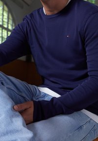 Granatowy sweatshirt z długim rękawem i okrągłym dekoltem, wykonany z miękkiej tkaniny, z małym logo na piersi, w połączeniu z jasnoniebieskimi dżinsami.