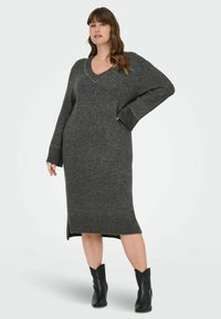 Grå stickad klänning med v-ringning, långa ärmar och sidoklyftor. Utsmyckad med dekorspikar längs halsringningen och ärmsluten. Buren med svarta ankelskor.