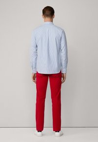 Camisa de rayas azul claro con mangas largas, combinada con pantalones rojos brillantes. La camisa cuenta con un cuello puntiagudo y un botón en la parte posterior.