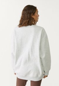 Oversized grå sweatshirt med rund halsringning och ribbad manschett. Mjuk textur med ett subtilt melerat mönster, bärs med bruna byxor.