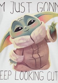 T-shirt bianco con un personaggio dei cartoni animati dalle grandi orecchie, che indossa un cappotto marrone con un colletto chiaro, e del testo sopra in carattere scuro.