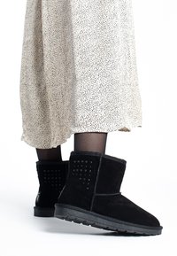 Botines de ante negro con detalles de tachuelas, parte superior texturizada y suela de goma. Combinados con una falda ligera con estampado y pantys negros transparentes.