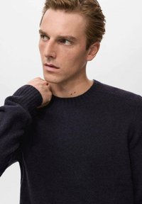 Temno modra pulover iz mehkih materialov, z okroglim izrezom in rebrastimi manšetami. Ozek kroj z minimalnimi detajli.