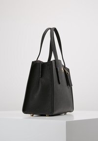 Czarna skórzana torebka o teksturowanym wykończeniu, z dwoma długimi uchwytami, w zdefiniowanym kształcie, ze złotymi akcentami i ochronnymi metalowymi nóżkami u podstawy.