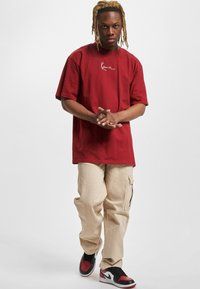 Rød bomulds oversized t-shirt med hvidt logo, parret med lysebeige cargo-bukser med sidelomme og sorte og røde sneakers.