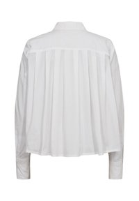 Chemise blanche à manches longues avec plis dans le dos, col classique et poignets boutonnés sur fond uni.