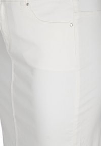 Gros plan sur un jean en denim blanc montrant la poche avant, les rivets, les passants de ceinture et les détails de couture sur le tissu.