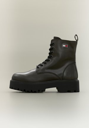 Bottine noire en cuir à lacets, avec une semelle épaisse à crampons, un écusson logo sur le côté et une bride arrière.