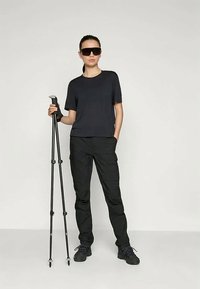 Black short-sleeve t-shirt and cargo pants, with a person holding black trekking poles. Sunglasses and rugged footwear complete the outdoor look.